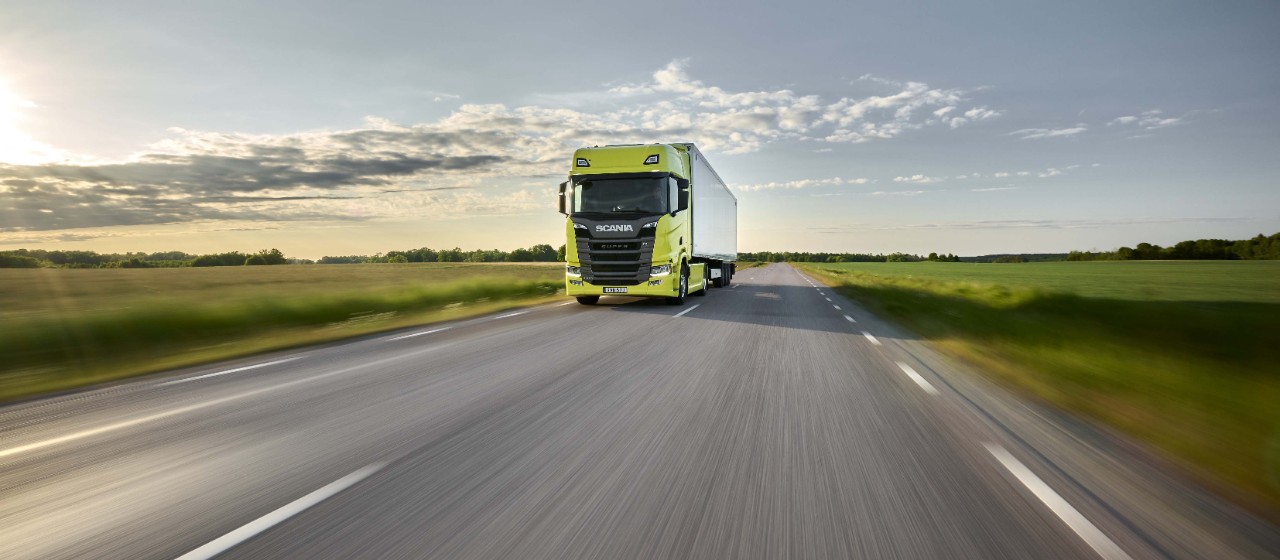 Ein gelber Scania-LKW auf einer von grünen Feldern umgebenen Straße