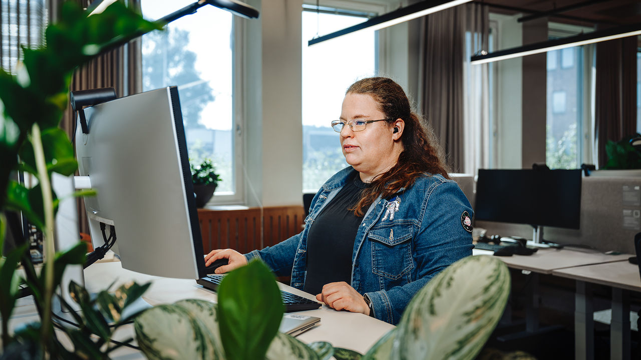 A picture of Evy Svensson, Enterprise Architect at Scania. She is sitting behind a desk at one of Scania's offices, working from her computer.
