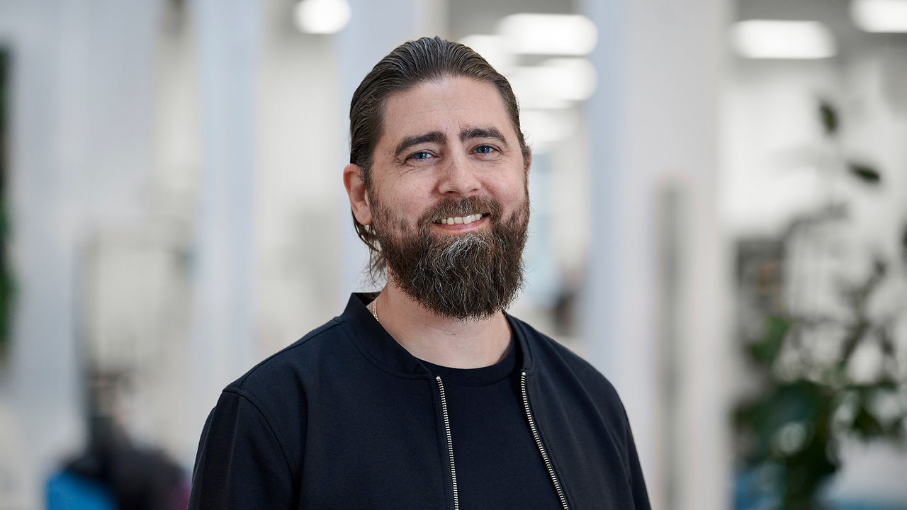 A portrait of Daniel Frylmark, a Solutions Manager at TRATON Group R&D, in an office environment. Daniel is smiling.
