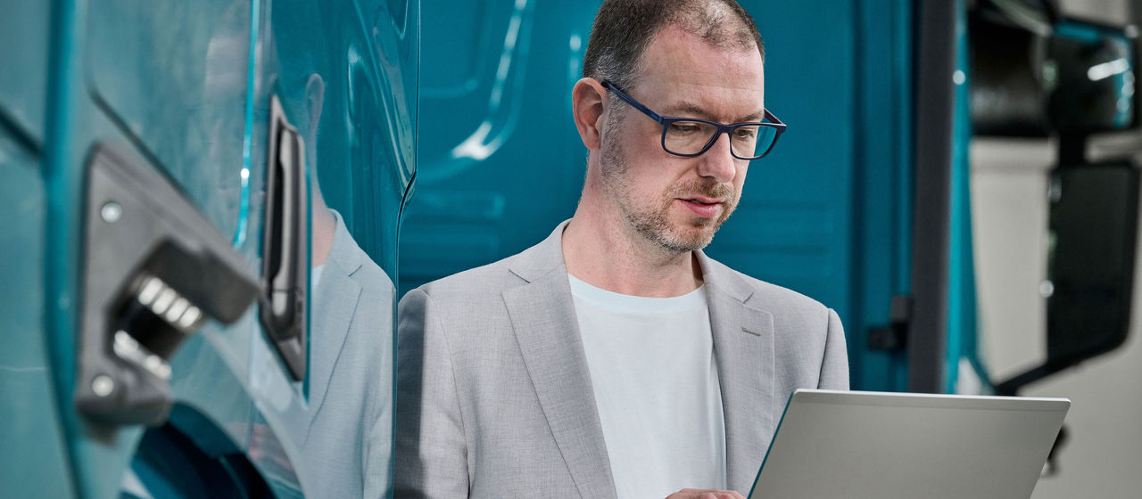 Daniel Blank, Product Manager within the hub-to-hub workstream at TRATON Group R&D. He's standing infront of a Scania autonomous truck, looking at his laptop.